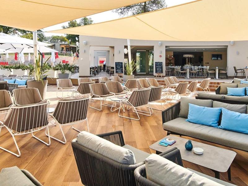 Terrasse extérieure moderne avec coin salon confortable, tables et auvents dans un cadre lumineux.