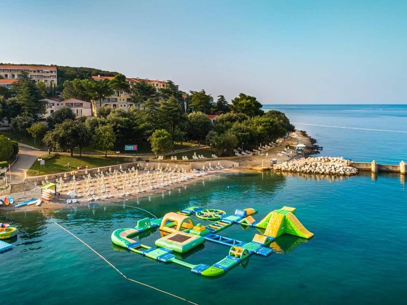 Parc aquatique avec toboggans dans une mer bleue calme devant un hôtel côtier.