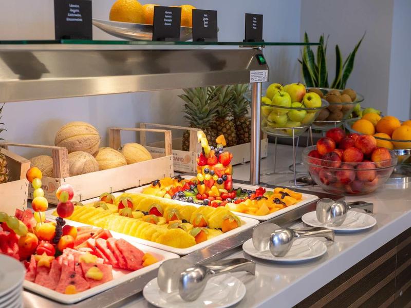 Buffet avec des fruits frais, melons, pommes et salades de fruits sur un comptoir blanc.