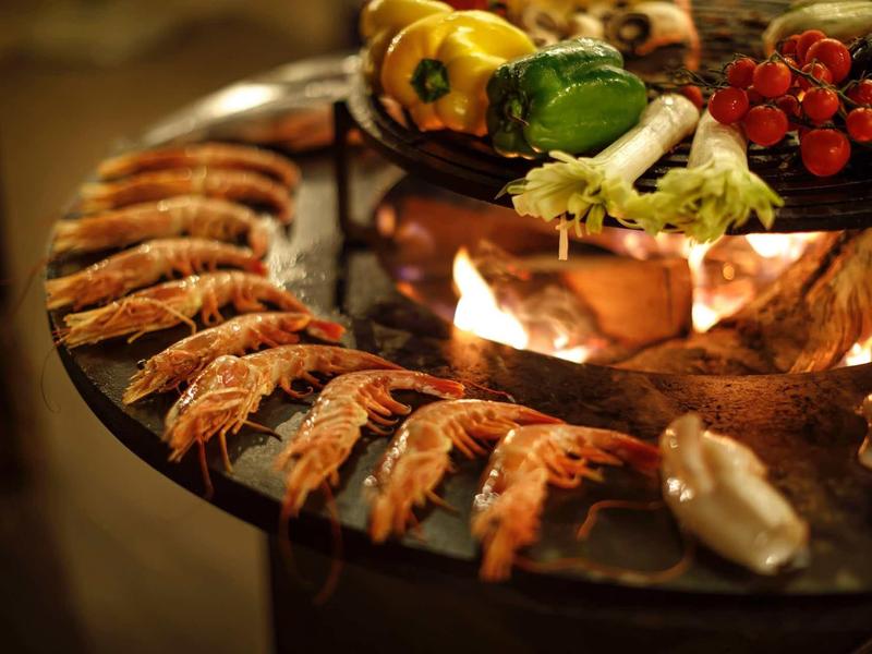 Crevettes fraîches et légumes sur un gril rond avec un feu de bois.