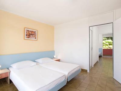 Una habitación de hotel sencilla con dos camas individuales, lámparas de noche y vista a un pasillo.