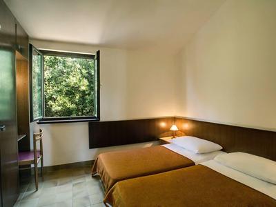 Una habitación de hotel sencilla con dos camas individuales, una ventana abierta y una pequeña silla.