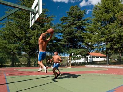Deux hommes jouent au basket-ball sur un terrain extérieur avec des arbres en arrière-plan.