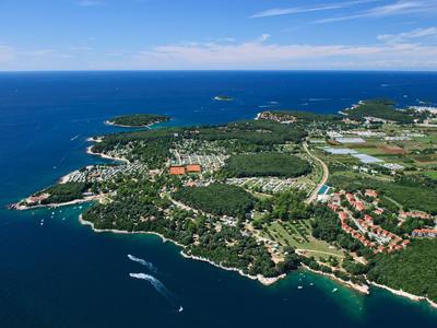 Luftaufnahme einer grünen Halbinsel mit Hotels entlang der Küste und blauem Meer.