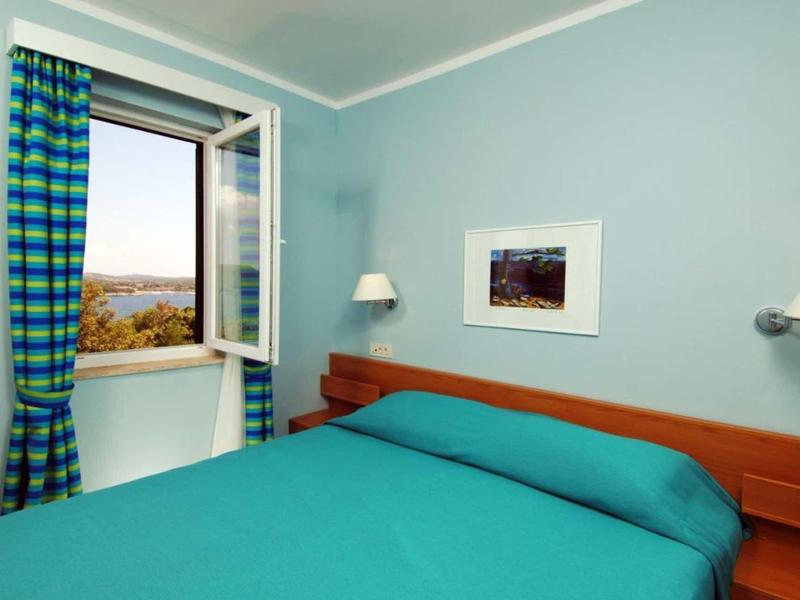 Jasnoniebieska sypialnia z podwójnym łóżkiem i otwartym oknem z widokiem.