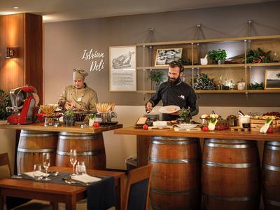 Gemütliches Restaurant mit Holzfässern als Tische, zwei Köche bereiten Speisen zu, warme Beleuchtung.