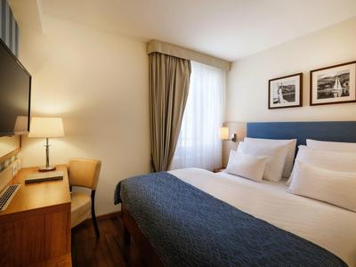 Pohodlný hotelový pokoj s dvoulůžkem, psacím stolem, židlí a okenními závěsy