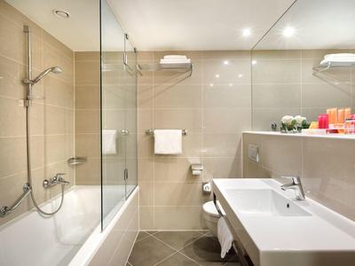 Moderní koupelna s vanou, skleněnou sprchovou stěnou, umyvadlem a ručníky.