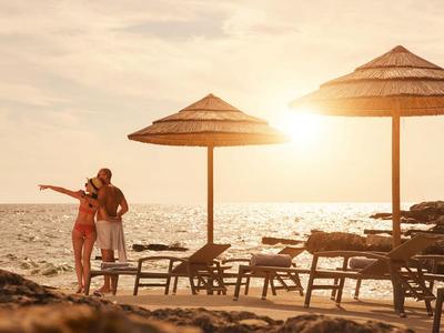 Koppel staat op het strand bij zonsondergang naast ligstoelen en parasols.