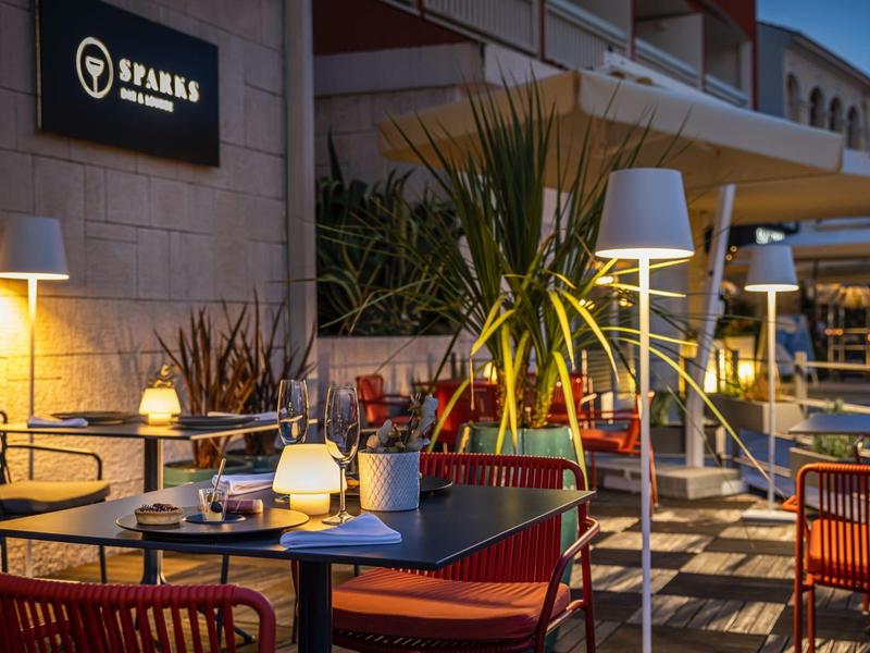 Pohodlná venkovní terasa restaurace se stoly, červenými židlemi a atmosférickým osvětlením.