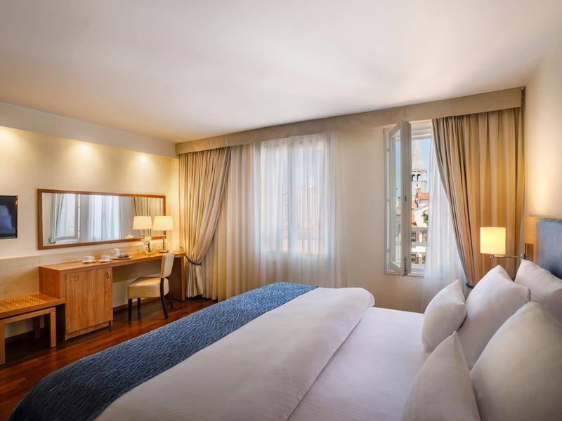 Moderní hotelový pokoj s manželskou postelí, psacím stolem, televizí a teplým osvětlením.