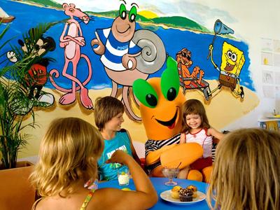 Bambini che mangiano davanti a una parete con cartoni animati colorati in una zona hotel adatta ai bambini.