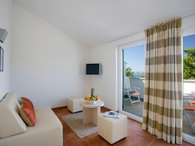 Soggiorno luminoso con divano, TV, piccolo tavolo e accesso al balcone con vista sul giardino.