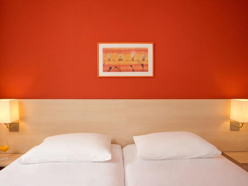 Camera d'hotel con due letti singoli, parete rossa e due lampade da parete.