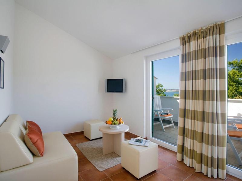 Soggiorno luminoso con divano, TV, piccolo tavolo e accesso al balcone con vista sul giardino.