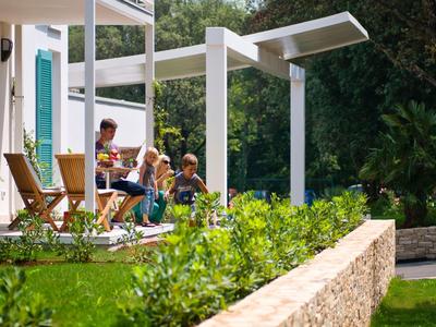 Mensen ontspannen op een terras van een modern vakantiehuis met uitzicht op de tuin.