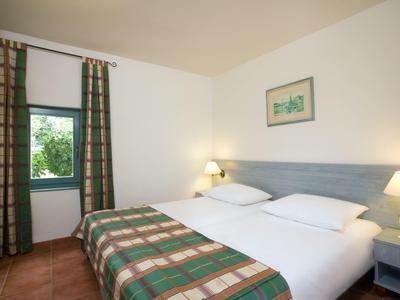 Une chambre d'hôtel simple avec deux lits simples, des tables de chevet et une fenêtre avec des rideaux.