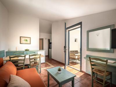 Světý obývací pokoj s oranžovou pohovkou, zeleným stolem, židlemi a přístupem na balkon.