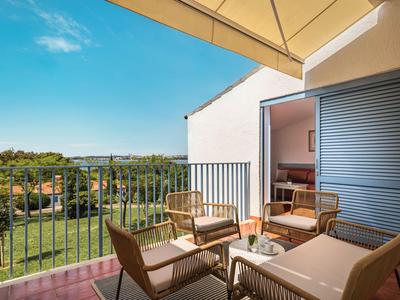 Balkon s židlemi a stolem s výhledem na zelenou krajinu pod jasnou oblohou.