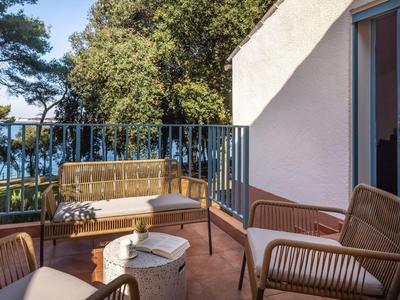 Balkon s proutěnými židlemi, pohovkou a stolem s výhledem na stromy a vodu.