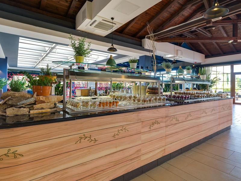 Espace bar d'hôtel moderne avec comptoir en bois et étagères en verre remplies de plantes et bouteilles.