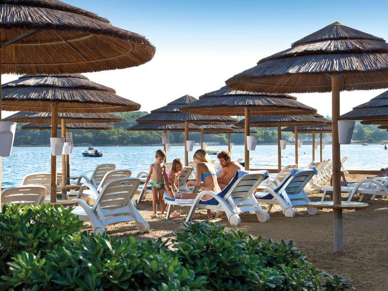Plage avec chaises longues, parasols et personnes se relaxant au bord de l'eau.