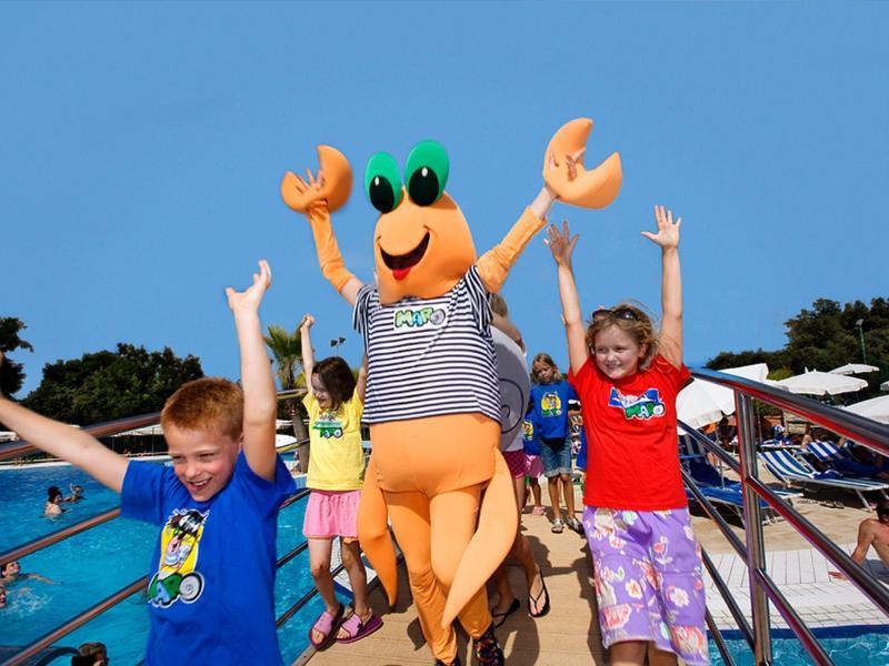 Des enfants jouent près de la piscine avec une mascotte crabe, s'amusant pendant les vacances.