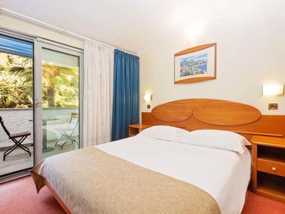 Chambre d'hôtel confortable avec lit double, tables de nuit et accès à un balcon avec vue sur les arbres.