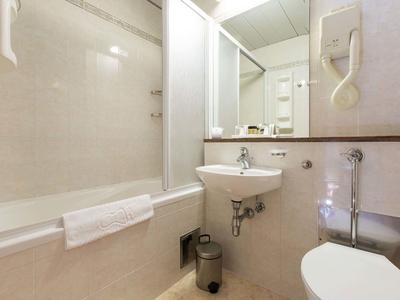 Petite salle de bain avec baignoire, lavabo, toilettes et sèche-cheveux mural.