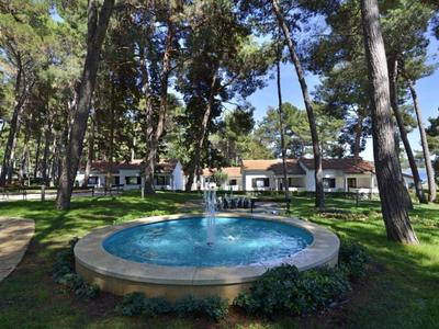 Fontaine avec eau jaillissante dans un parc avec des arbres devant un bâtiment par une journée ensoleillée.