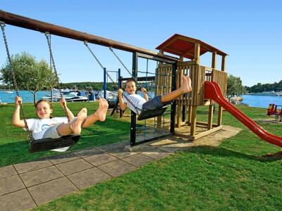 Des enfants se balancent et jouent sur une aire de jeux dans un parc par temps clair.