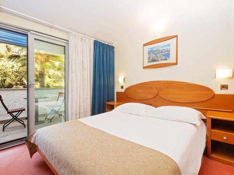 Chambre d'hôtel confortable avec lit double, tables de nuit et accès à un balcon avec vue sur les arbres.