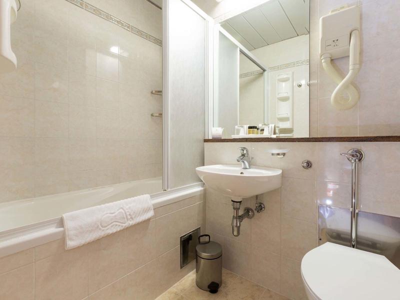 Petite salle de bain avec baignoire, lavabo, toilettes et sèche-cheveux mural.