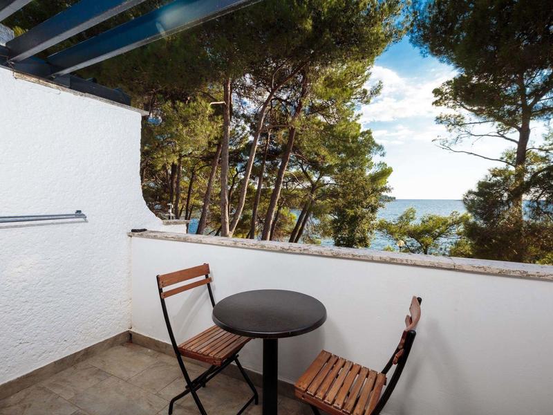 Petit balcon avec deux chaises, une table ronde et vue sur les arbres et la mer.