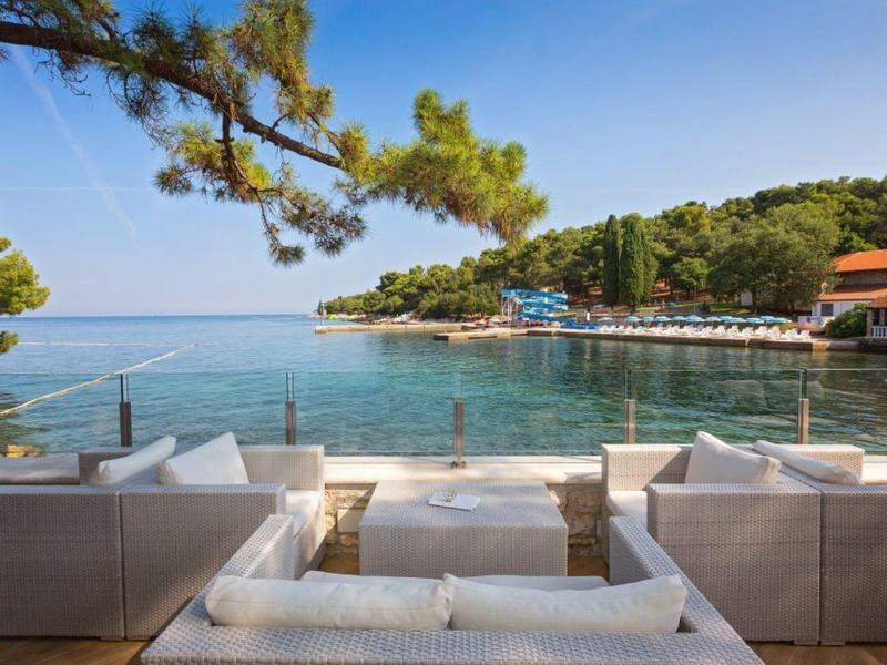 Vue depuis une terrasse avec des canapés blancs sur une baie calme et des collines boisées.