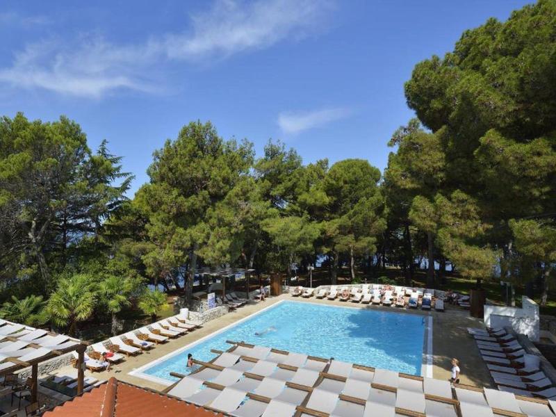 Piscine extérieure avec chaises longues entourée de grands arbres et ciel bleu.
