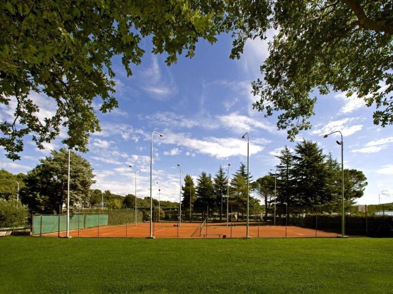Terrain de tennis en terre battue en plein air entouré d'arbres sous un ciel bleu