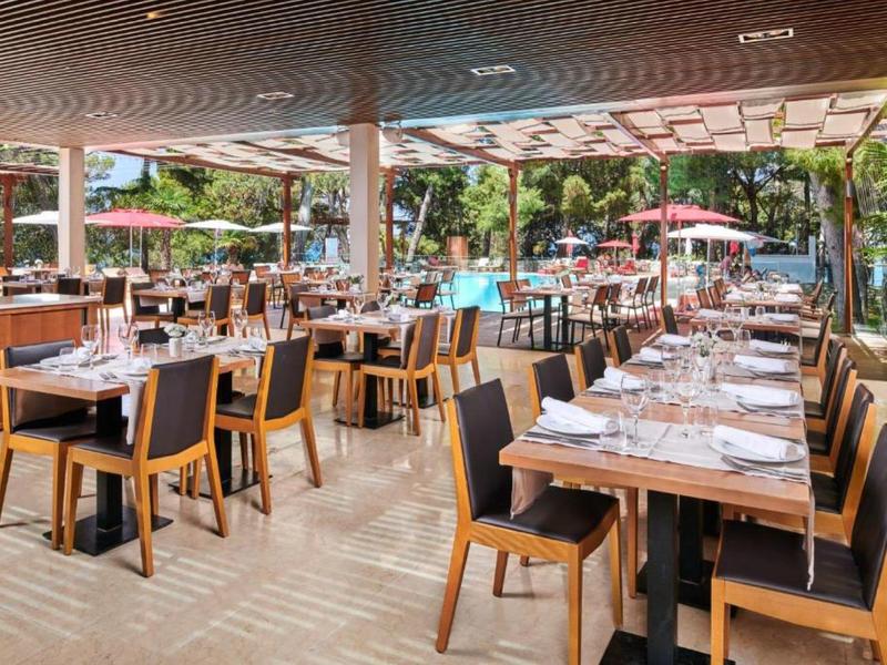 Restaurant lumineux avec de nombreuses tables et chaises en bois dressées à côté d'une piscine.