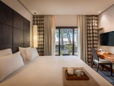 Modernes Hotelzimmer mit großem Bett, Schreibtisch und Blick auf Terrasse und Bäume.