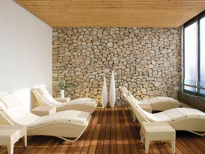 Area lounge rilassante con poltrone crema, muro in pietra, pavimento in legno e grandi finestre