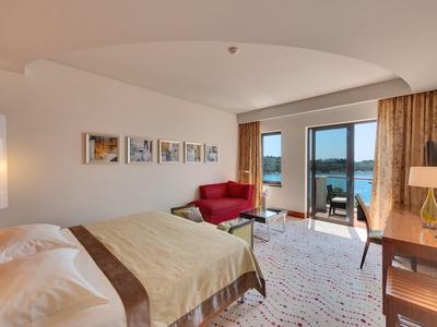 Camera d'hotel moderna con letto matrimoniale, area salotto, scrivania e balcone con vista sul lago.