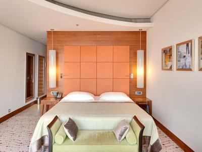 Camera d'hotel moderna con grande letto, testiera in legno e divano a piedi del letto.