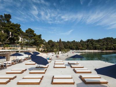 Tumbonas modernas con sombrillas azules en una playa tranquila junto a agua clara.