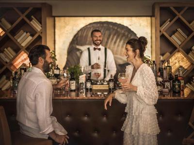 Un hombre y una mujer hablan en un bar mientras el barman sonríe y está listo.