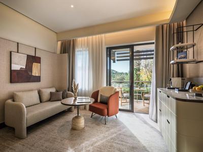Modernes Wohnzimmer mit Sofa, Sessel, Teppich und Zugang zu einem Balkon mit Aussicht.