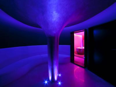 Modernes Hotelfoyer mit geschwungener Säule und violett-blauer Beleuchtung bei Nacht.