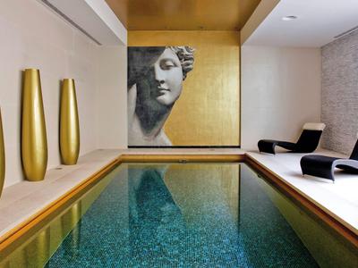 Innenpool mit goldfarbenen Vasen, zwei schwarzen Liegestühlen und Kunstwerk an der Wand.