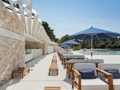 Moderner Außenbereich mit Sonnenliegen und blauen Sonnenschirmen an einem Hotelpool.