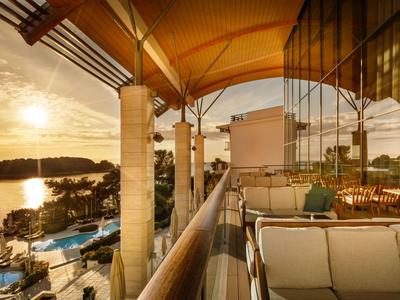 Balkon mit Sitzgruppe in einem Hotel mit Blick auf Wasser und Sonnenuntergang.