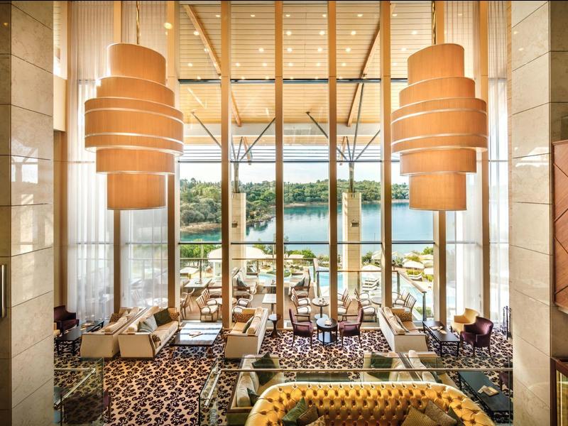 Ampia hall d'hotel con grandi finestre, illuminazione moderna e posti a sedere con vista sull'acqua.